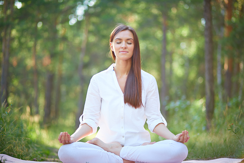 Portrait of calm woman sitting in pose of lotus in natural environment